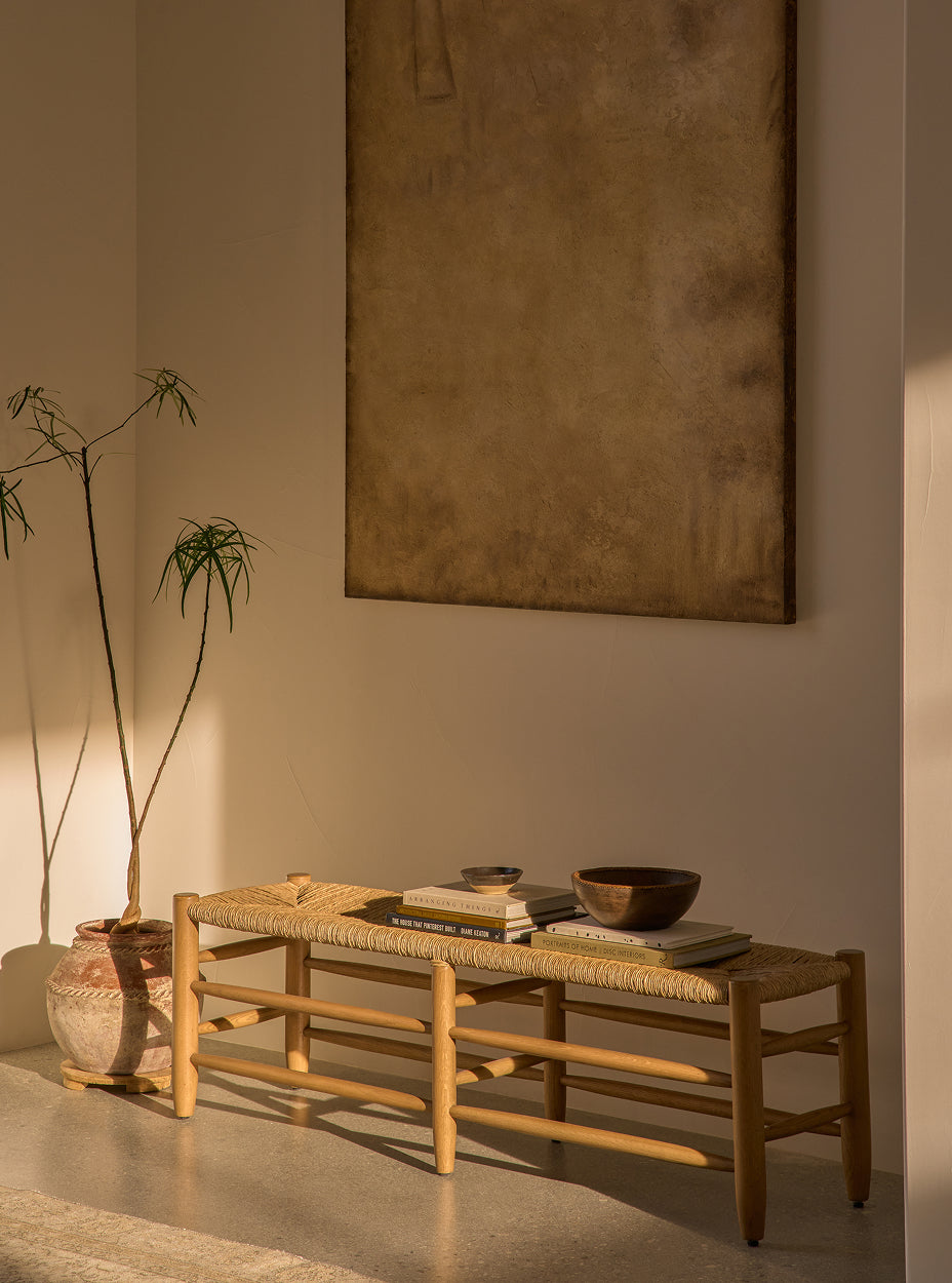The mina bench with books and a bowl in a room with a large abstract painting on the wall.