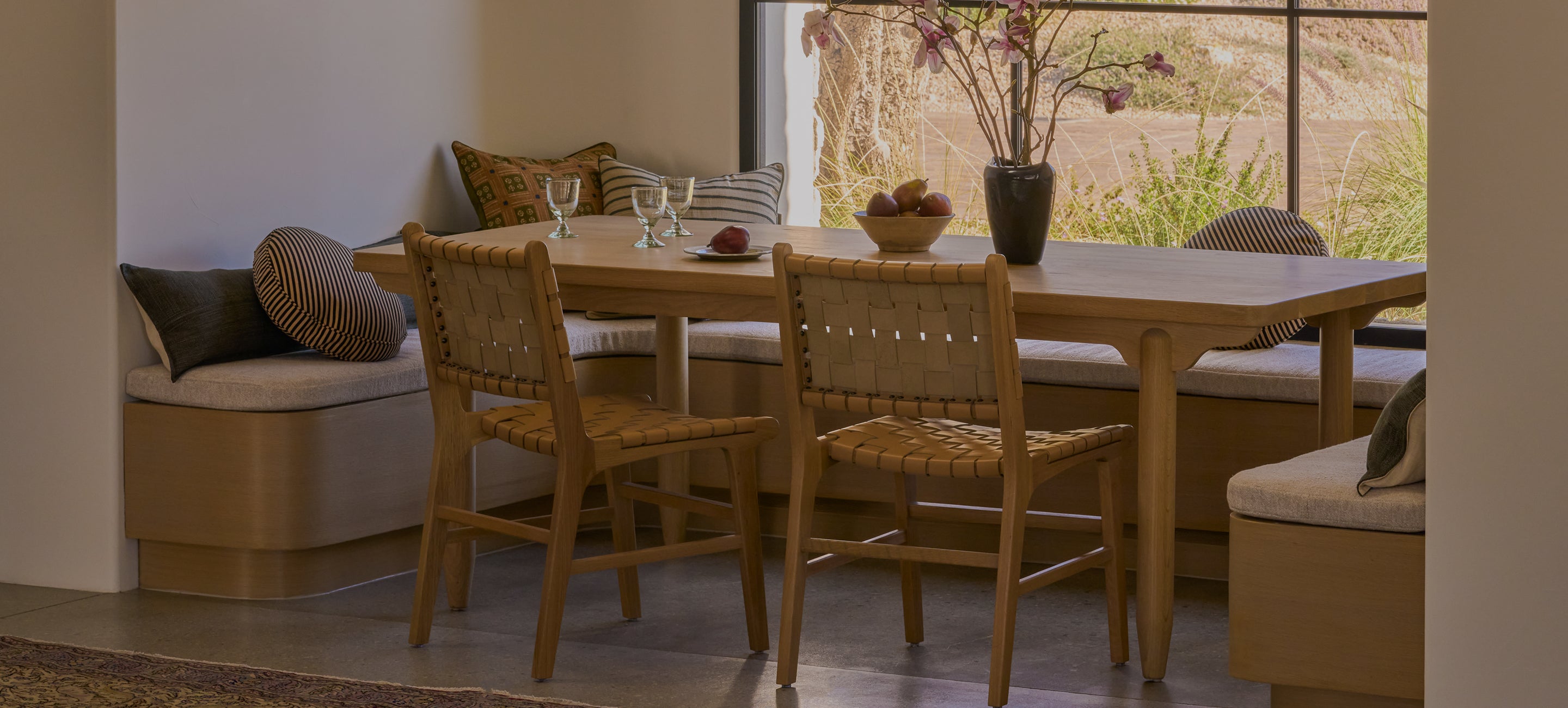 Dining area with wooden table and bali dining chairs in a bright room with large windows.