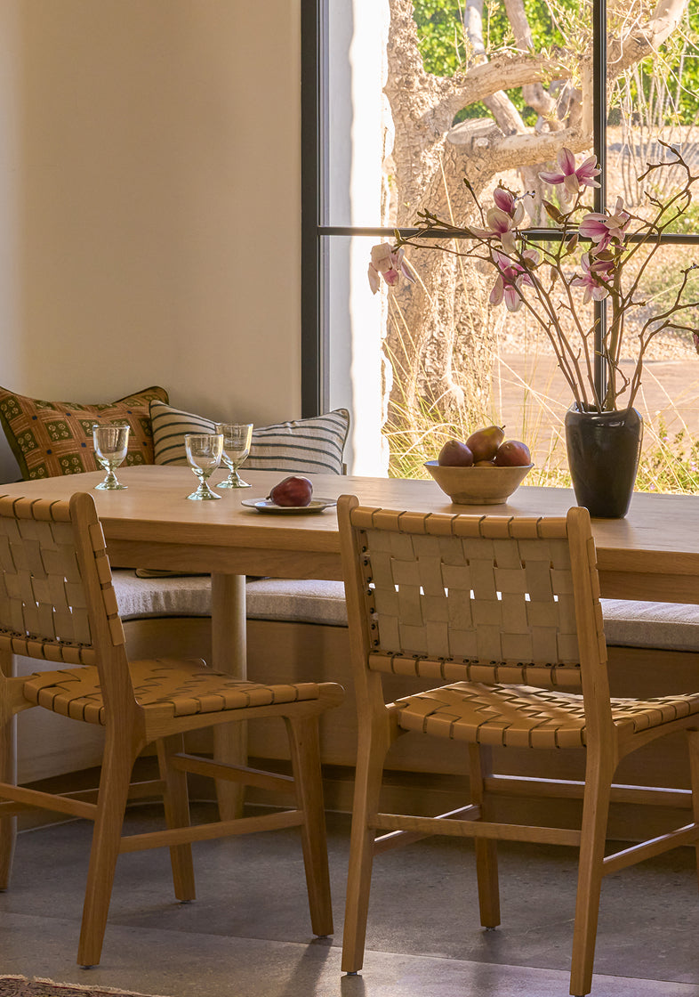 Dining area with wooden table and bali dining chairs in a bright room with large windows.