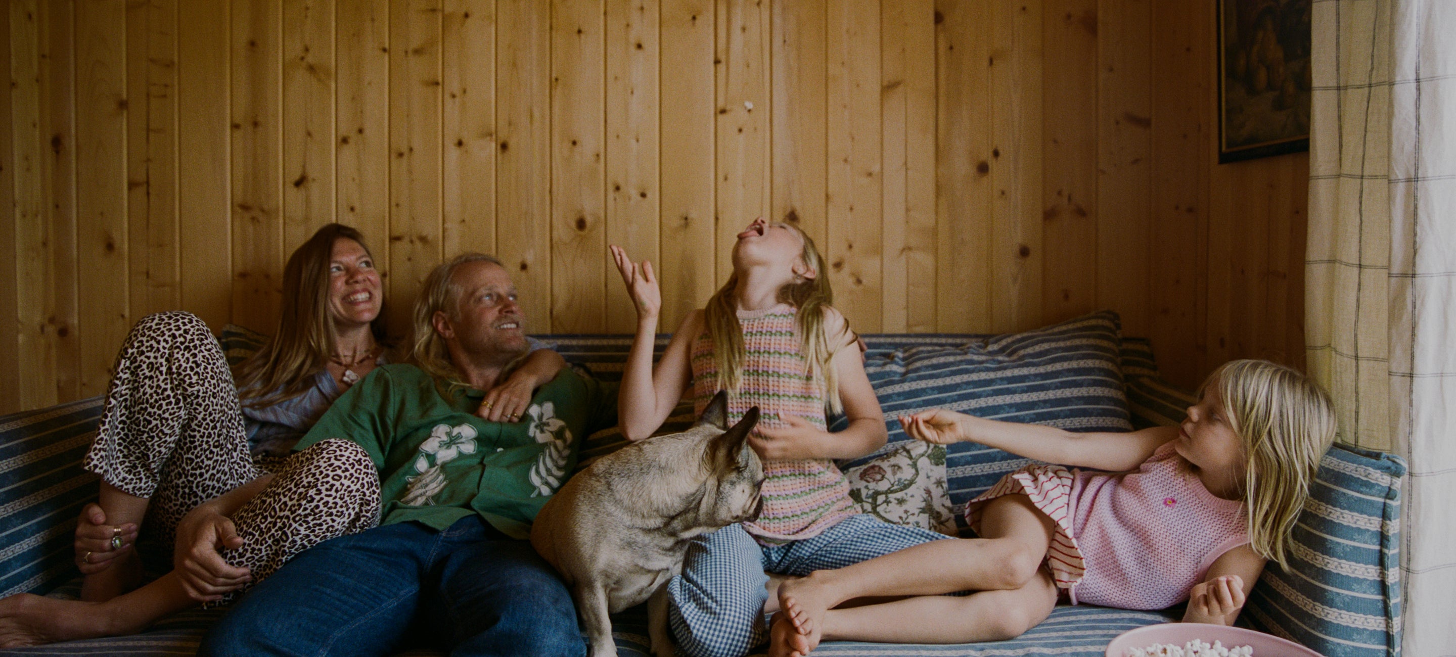 The Thomson's with a dog sitting on a striped couch in a wooden cabin.