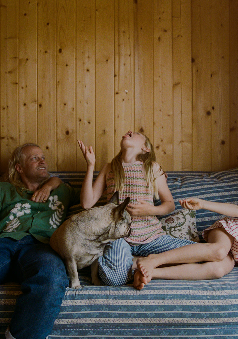 The Thomson's with a dog sitting on a striped couch in a wooden cabin.