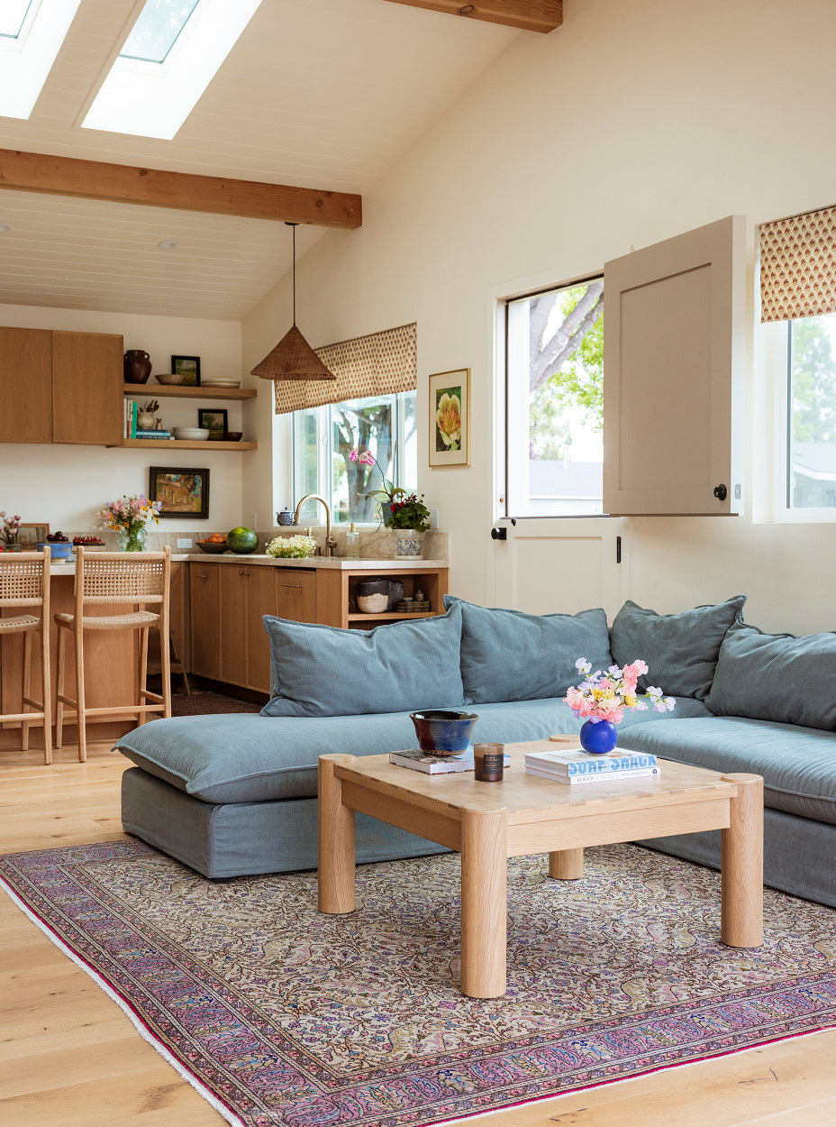 Modern living room with a gray sectional sofa, wooden coffee table, and kitchen area.