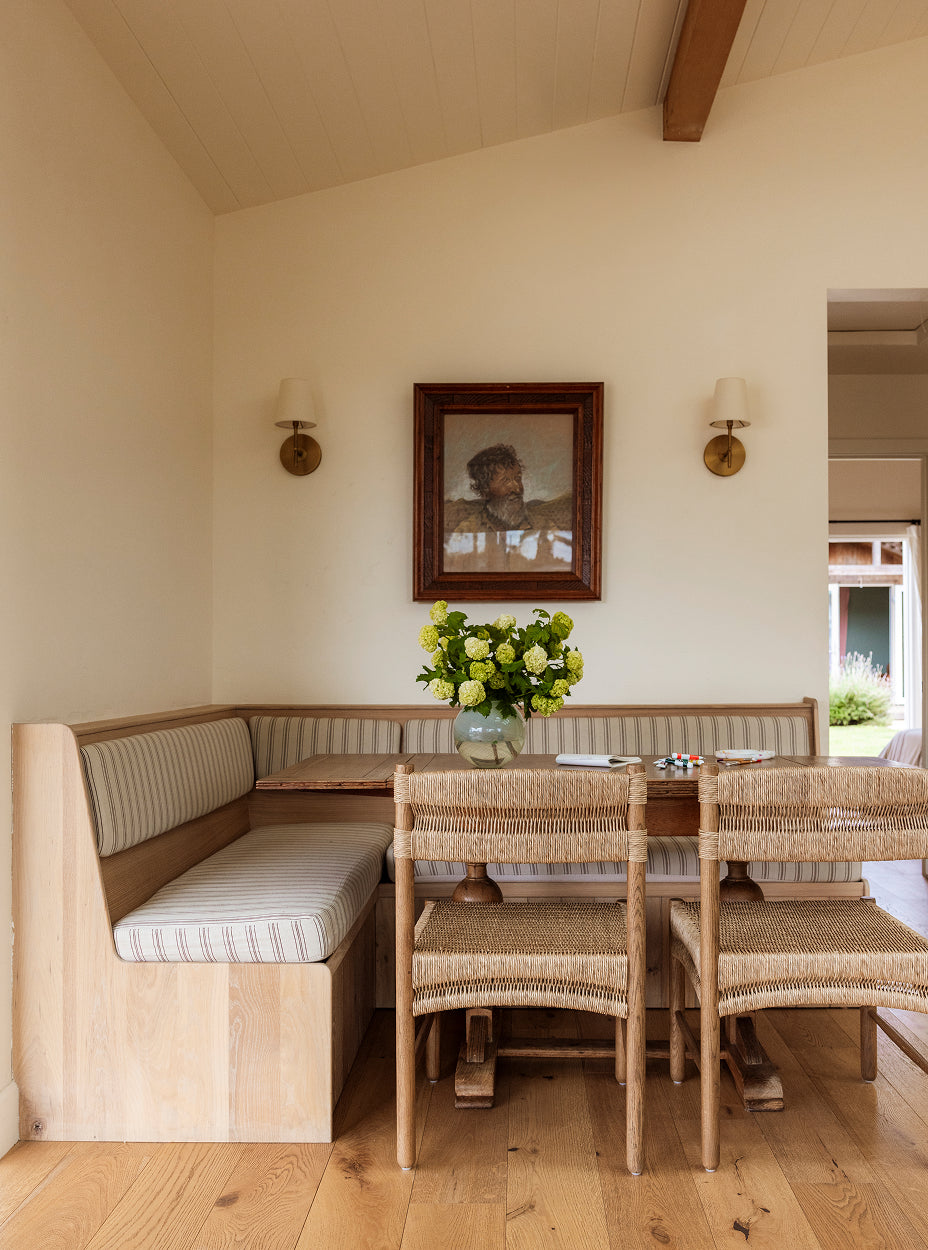 Dining area with wooden table, suma dining chairs, and a bench against a wall with a framed picture.