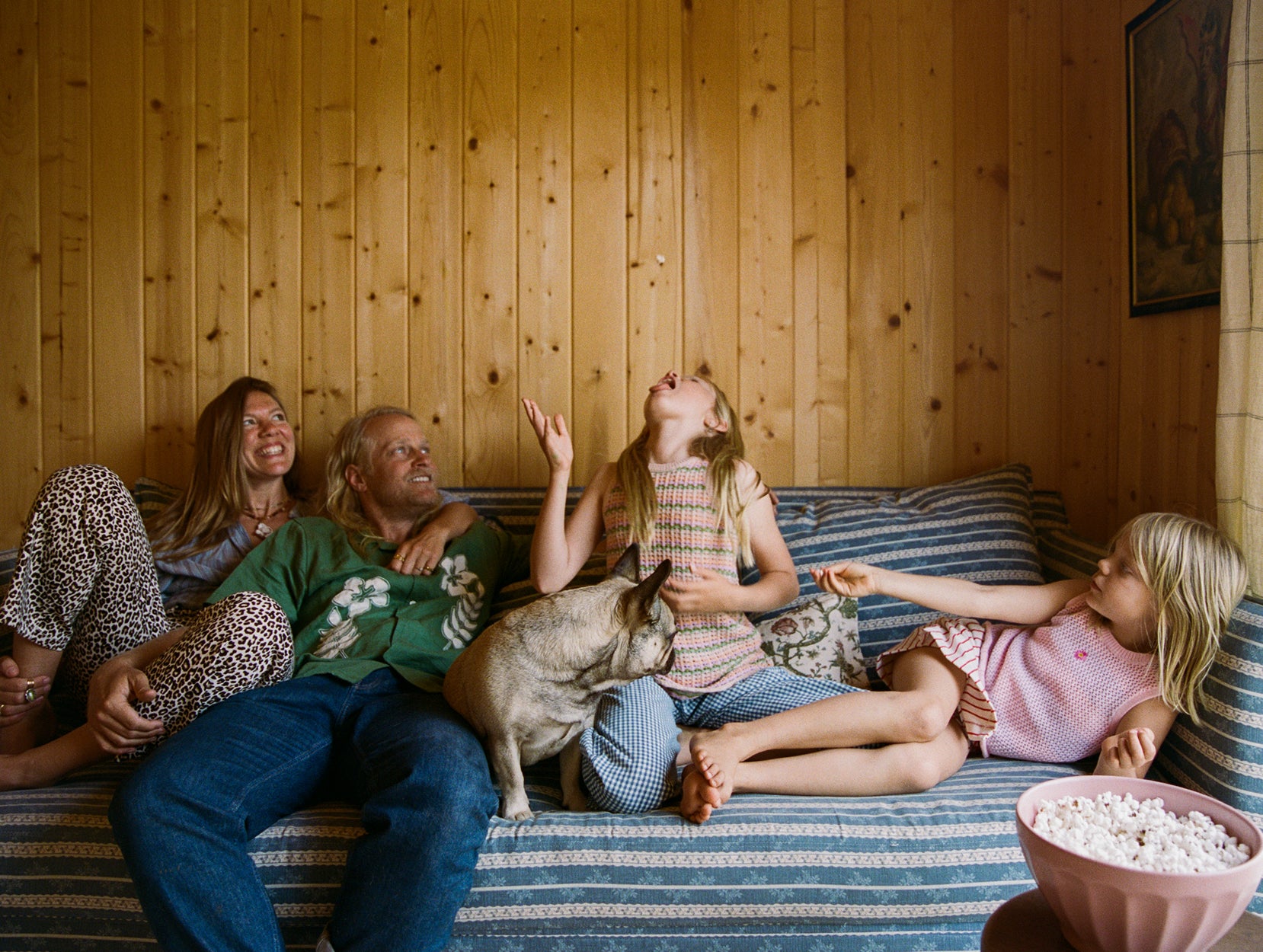 Thomson family sitting on a couch with a dog, eating popcorn in a cozy living room.