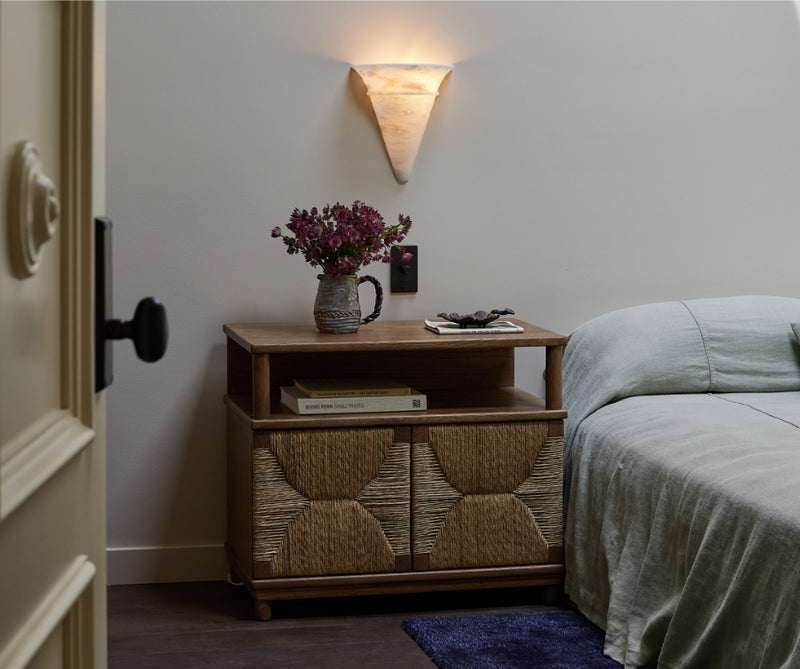 Bedroom with the Suma nightstand, made with oak and natural rush, floral arrangement, and books near a bed.
