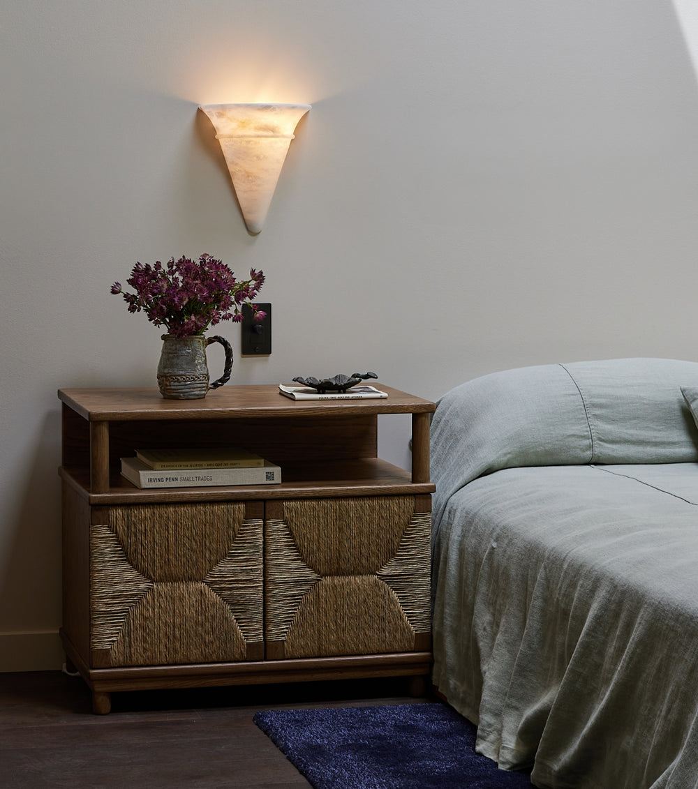 Suma, a oak and rush nightstand with decorative items next to a bed in a bedroom setting.